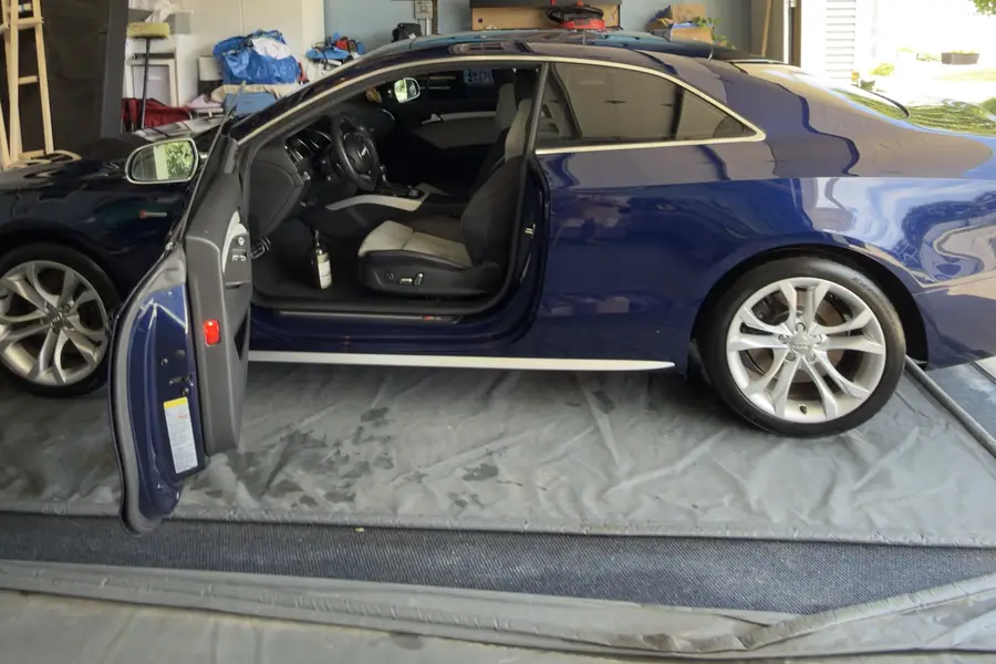 Dark blue Audi S5 coupe with the door open on a mat in a garage during a detail