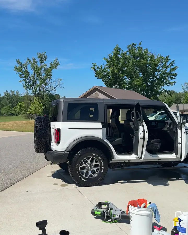 White Ford Bronco with the doors open in a driveway beside detailing equipment