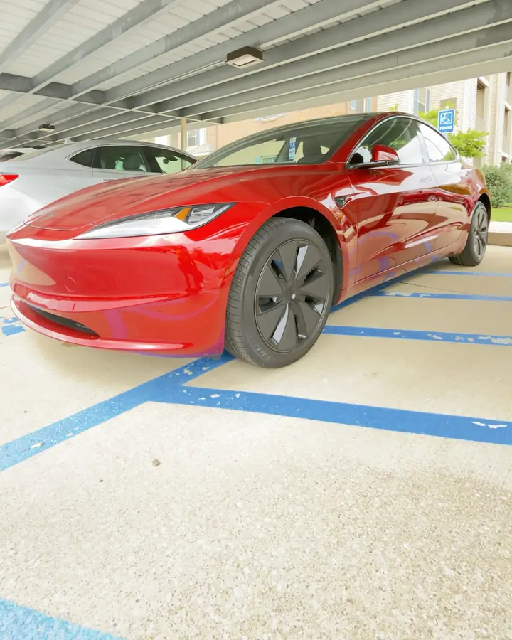 Front corner and wheel of a red Tesla Model 3 under a carport after ceramic coating in West Michigan