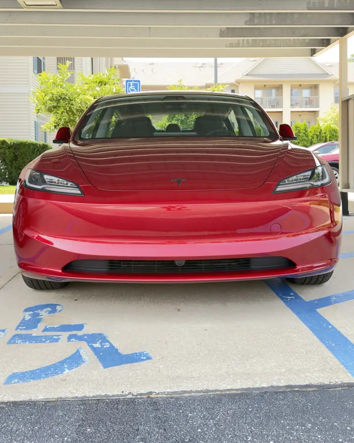 Front of a red Tesla Model 3 parked in a carport after ceramic coating, with even gloss across the bumper and hood