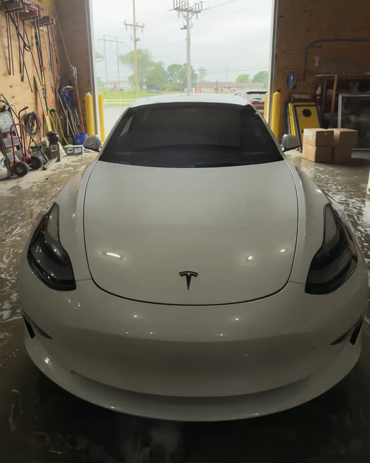 White Tesla sedan seen from the front after ceramic coating, parked in a garage bay